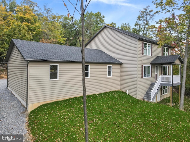 view of side of property with a yard, a shingled roof, and stairway