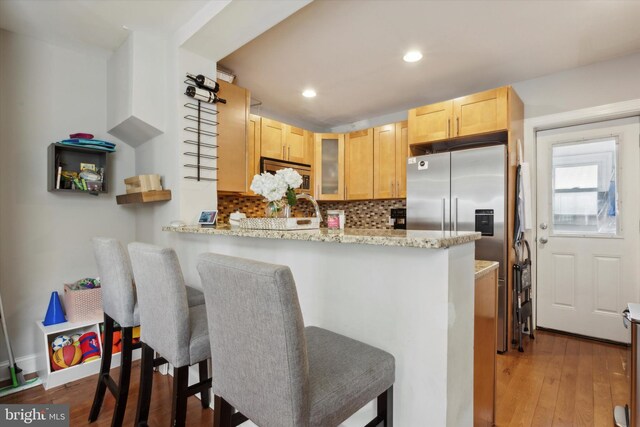 kitchen featuring light brown cabinetry, tasteful backsplash, light wood-type flooring, and kitchen peninsula