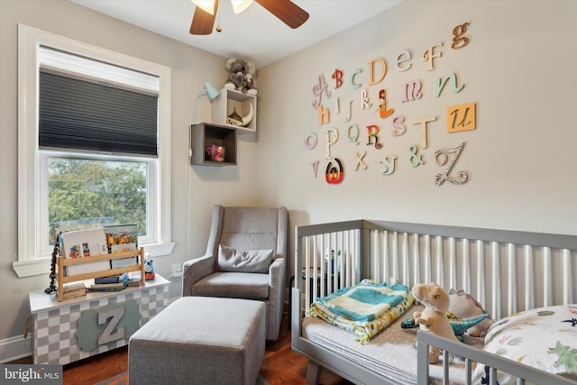 bedroom featuring a crib, dark hardwood / wood-style flooring, and ceiling fan