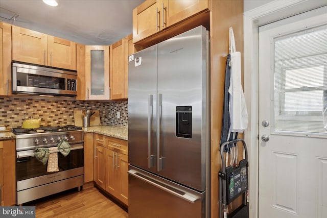 kitchen with decorative backsplash, light stone counters, light hardwood / wood-style flooring, and appliances with stainless steel finishes