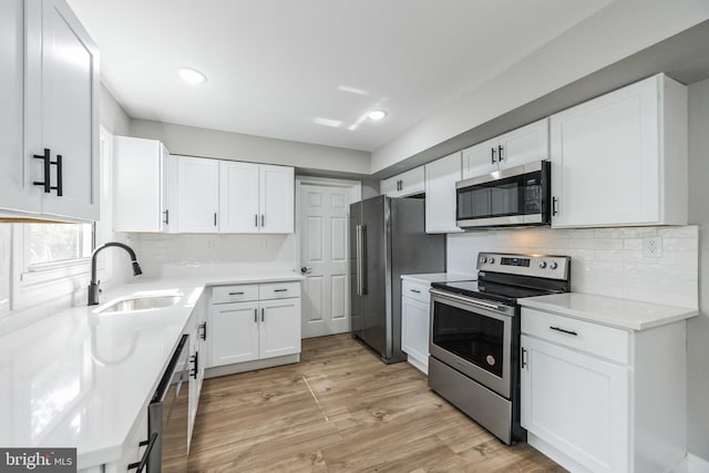 kitchen with appliances with stainless steel finishes, white cabinetry, sink, decorative backsplash, and light hardwood / wood-style flooring