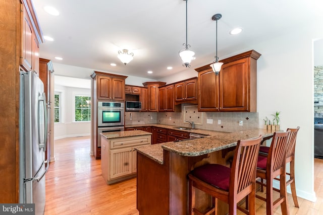 kitchen with appliances with stainless steel finishes, light wood-type flooring, a kitchen bar, and kitchen peninsula