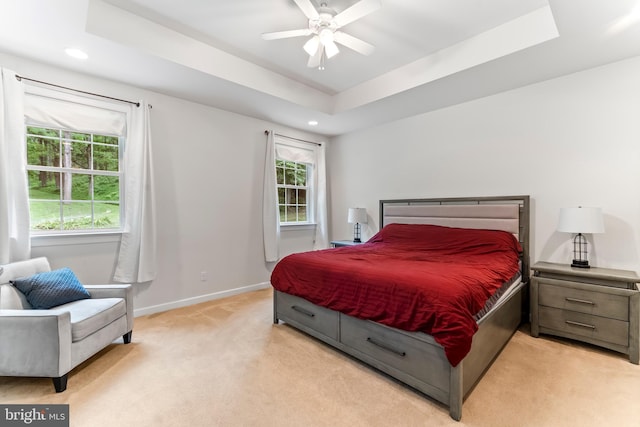 bedroom with ceiling fan, a raised ceiling, and light carpet