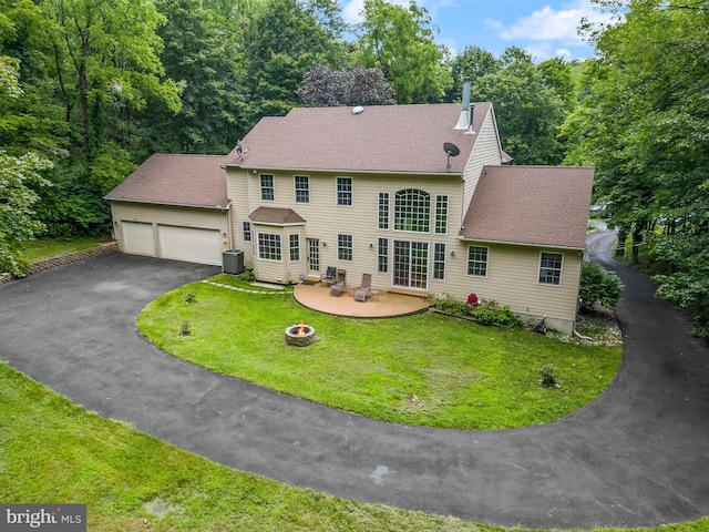 colonial inspired home with a fire pit, a front yard, a patio, central air condition unit, and a garage