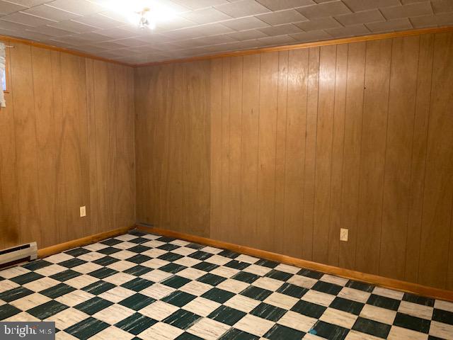 tiled empty room featuring wood walls and a baseboard radiator