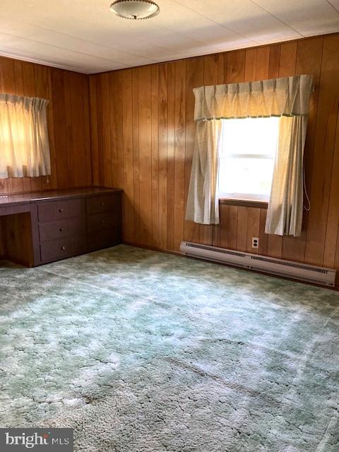 spare room with carpet floors, wooden walls, and a baseboard heating unit