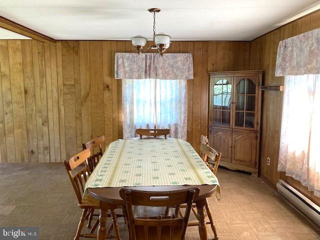 dining space with wooden walls, parquet flooring, a baseboard radiator, and a chandelier