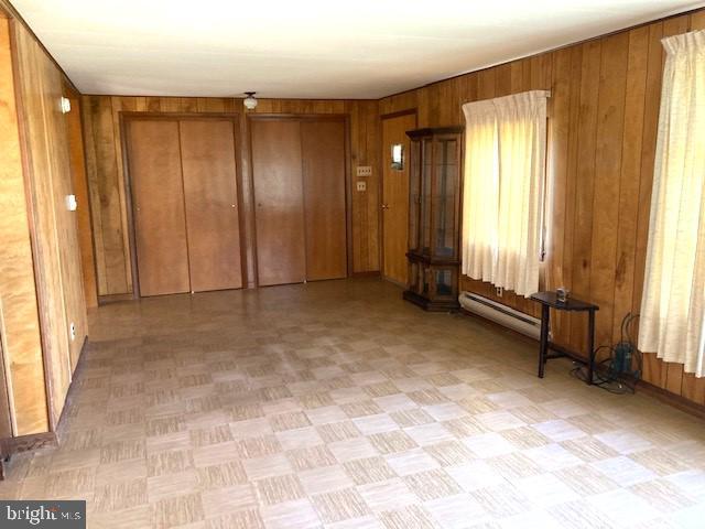 unfurnished room with wooden walls and a baseboard heating unit