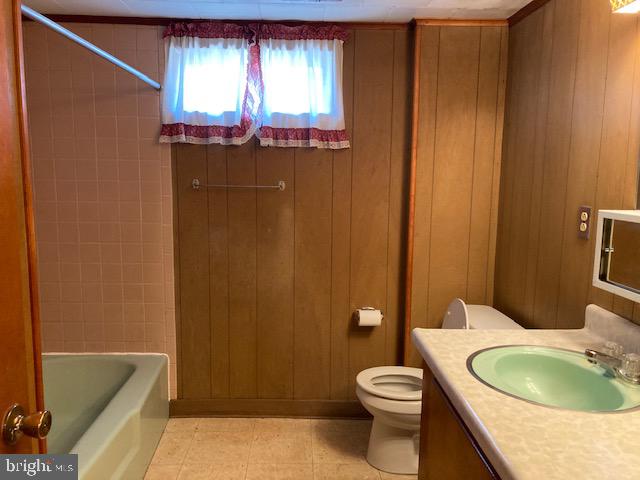 full bathroom featuring wooden walls, tiled shower / bath combo, toilet, vanity, and tile patterned floors