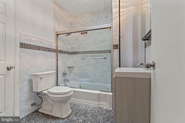 full bathroom featuring toilet, bath / shower combo with glass door, tile walls, vanity, and tile patterned flooring