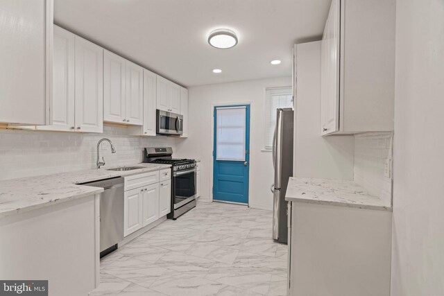 kitchen with appliances with stainless steel finishes, sink, white cabinets, and light stone counters