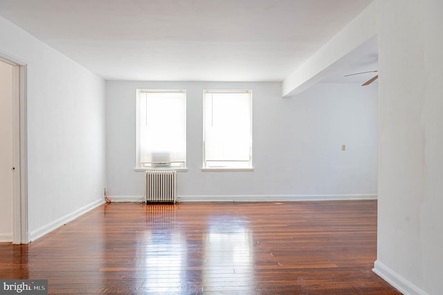 empty room with dark hardwood / wood-style flooring, ceiling fan, and radiator