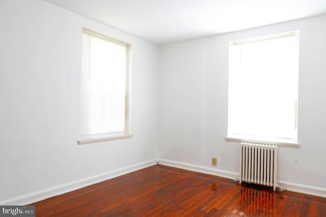 unfurnished room with a wealth of natural light, dark hardwood / wood-style floors, and radiator