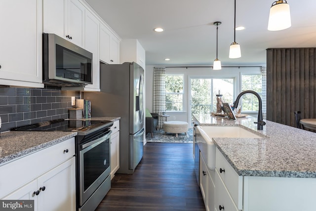 kitchen featuring tasteful backsplash, dark hardwood / wood-style flooring, an island with sink, appliances with stainless steel finishes, and decorative light fixtures