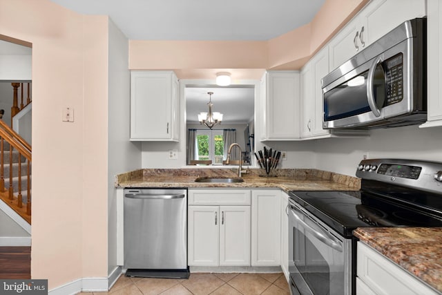 kitchen with a sink, an inviting chandelier, stone countertops, white cabinets, and appliances with stainless steel finishes