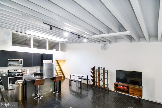 kitchen featuring beam ceiling, rail lighting, appliances with stainless steel finishes, hardwood / wood-style flooring, and a kitchen breakfast bar