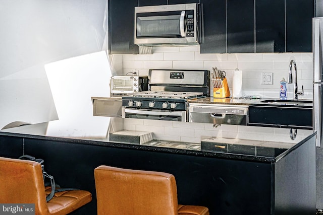 kitchen with sink, appliances with stainless steel finishes, decorative backsplash, and a kitchen breakfast bar