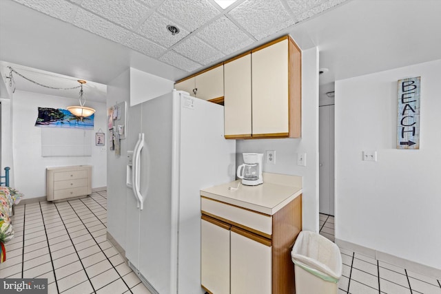 kitchen featuring light tile patterned flooring, a paneled ceiling, pendant lighting, white refrigerator with ice dispenser, and cream cabinetry