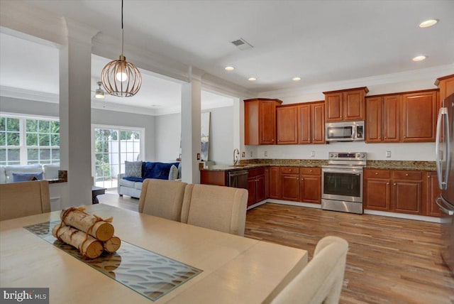 kitchen with hanging light fixtures, stone counters, crown molding, light wood-type flooring, and appliances with stainless steel finishes