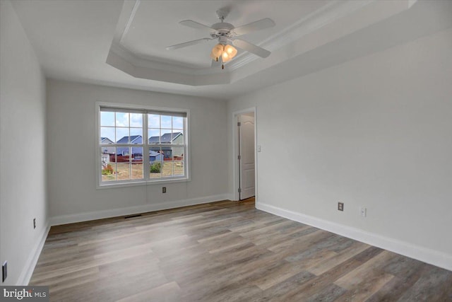 empty room with wood-type flooring, ceiling fan, and a raised ceiling