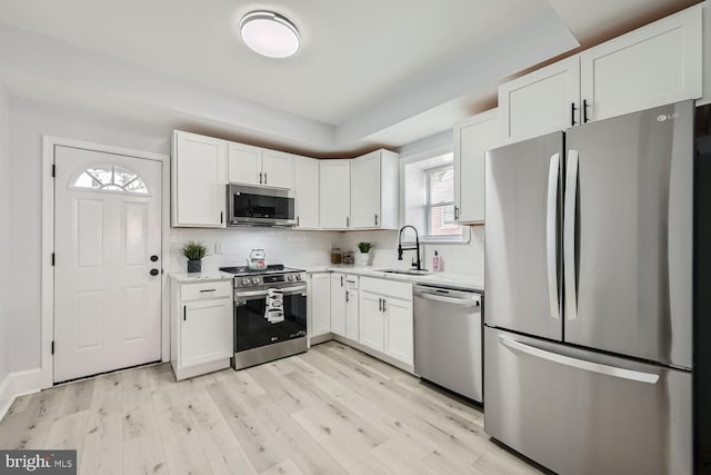 kitchen with sink, white cabinetry, tasteful backsplash, appliances with stainless steel finishes, and light hardwood / wood-style floors