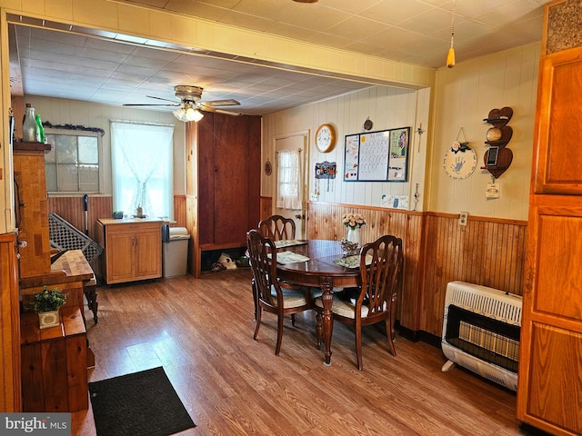 dining room featuring heating unit, wood walls, ceiling fan, and light hardwood / wood-style flooring