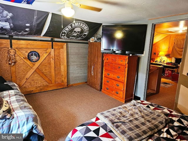 carpeted bedroom with a textured ceiling, ceiling fan, and wood walls