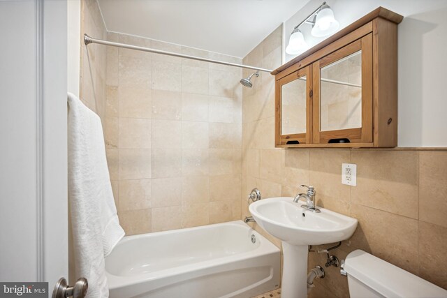 bathroom featuring backsplash, tiled shower / bath, toilet, and tile walls