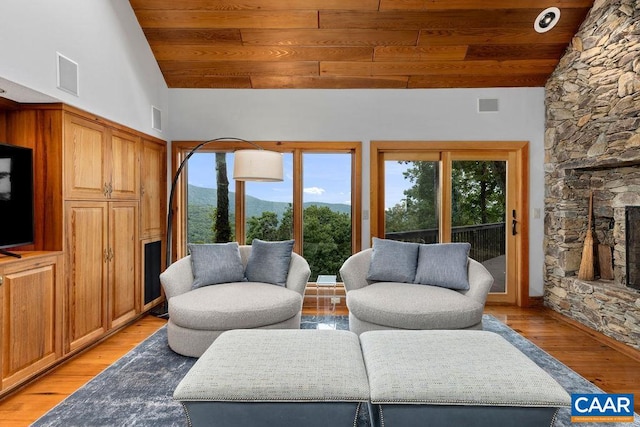 living room featuring a stone fireplace, light hardwood / wood-style floors, wood ceiling, and high vaulted ceiling