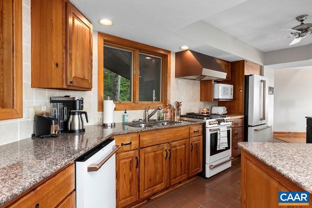 kitchen with white appliances, backsplash, ceiling fan, wall chimney exhaust hood, and sink