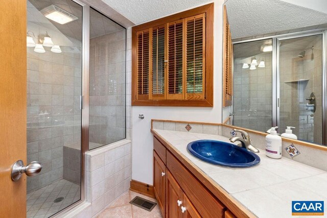 bathroom featuring a shower with door, vanity, a textured ceiling, and tile patterned flooring