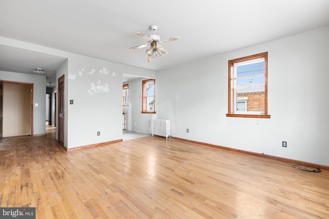 empty room with ceiling fan, light wood-type flooring, and radiator heating unit