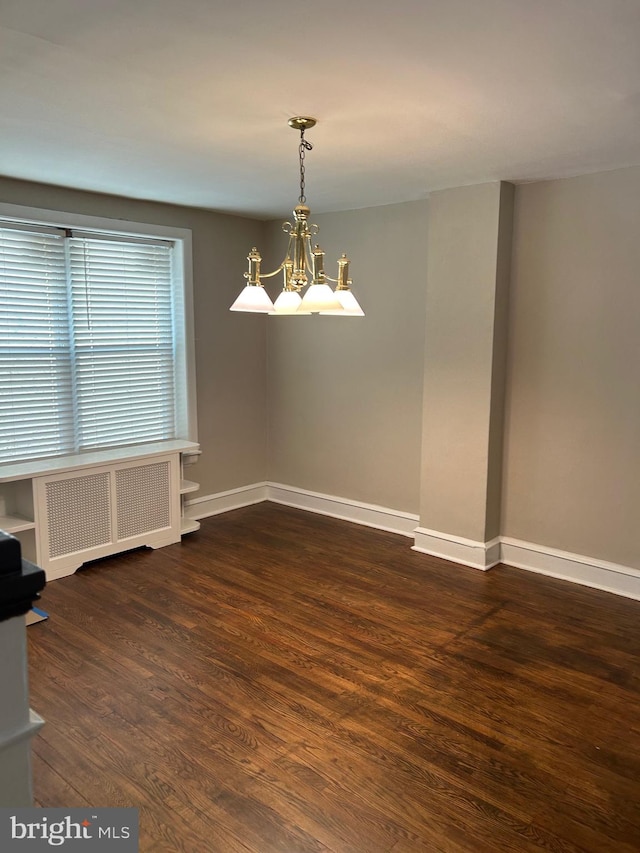 spare room with a notable chandelier, radiator, and dark wood-type flooring