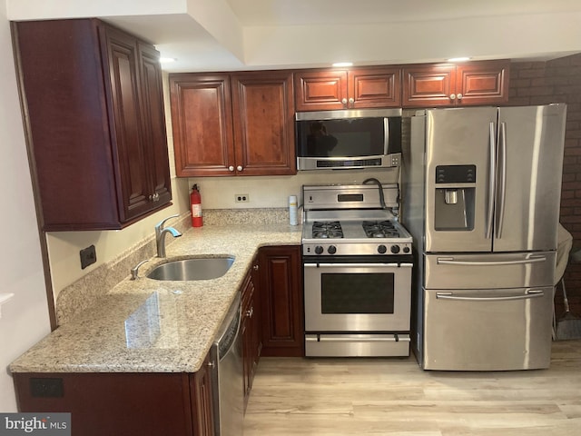 kitchen with sink, light stone countertops, stainless steel appliances, and light hardwood / wood-style floors