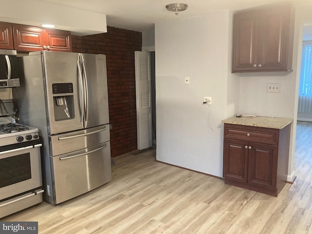 kitchen with brick wall, appliances with stainless steel finishes, light stone counters, and light hardwood / wood-style floors