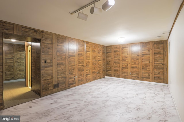 basement featuring marble finish floor, rail lighting, and wood walls