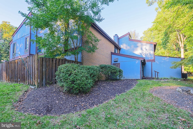 view of side of home featuring central AC unit, a lawn, a chimney, fence, and brick siding