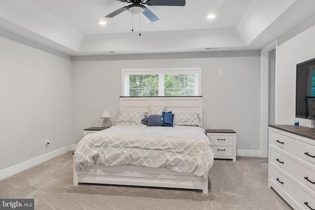 carpeted bedroom with ceiling fan and a tray ceiling