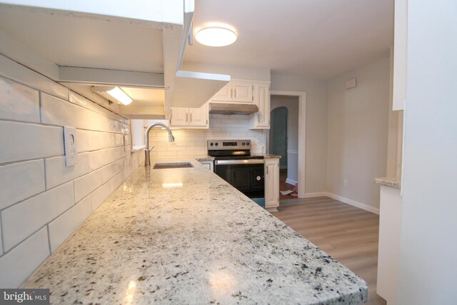 kitchen with white cabinets, light stone counters, backsplash, light wood-type flooring, and stainless steel range with electric stovetop