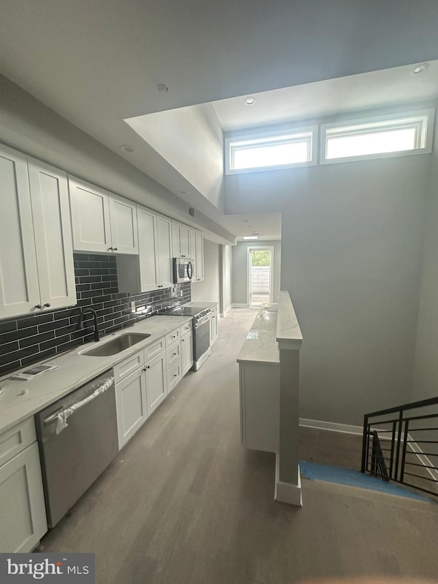 kitchen with white cabinets, sink, light hardwood / wood-style floors, appliances with stainless steel finishes, and backsplash