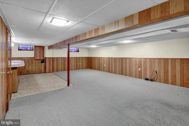 basement featuring carpet, a paneled ceiling, and wooden walls