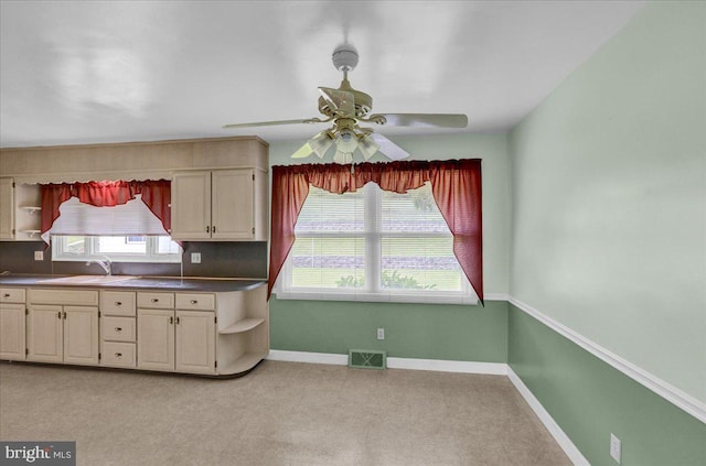 kitchen featuring sink, light carpet, ceiling fan, and cream cabinetry