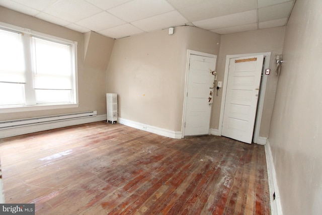 spare room with baseboard heating, radiator, hardwood / wood-style floors, and a drop ceiling