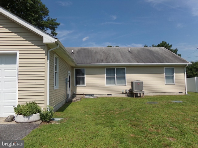 rear view of house featuring a garage, a lawn, and central AC