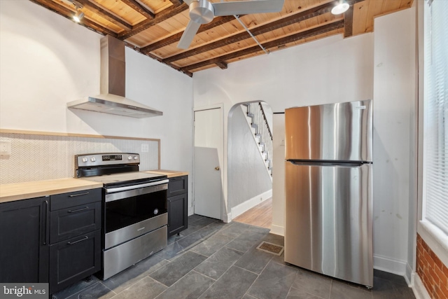 kitchen with beam ceiling, wall chimney range hood, stainless steel appliances, ceiling fan, and wooden ceiling