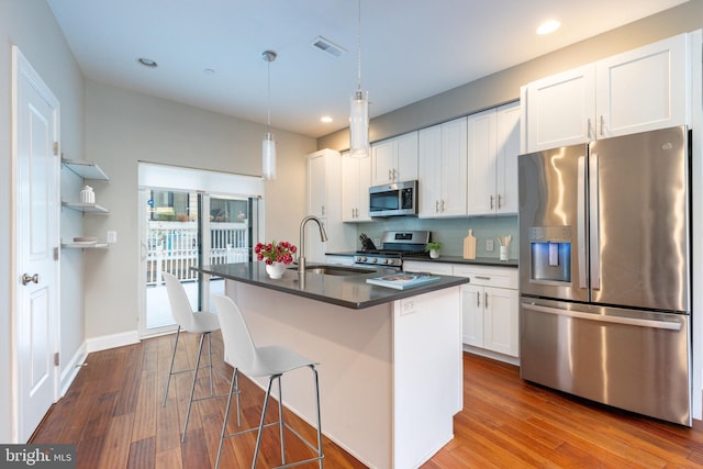 kitchen with a breakfast bar, appliances with stainless steel finishes, hardwood / wood-style flooring, a kitchen island with sink, and white cabinets