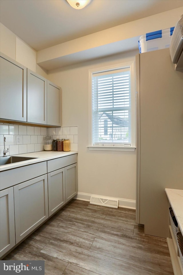 kitchen featuring backsplash, light hardwood / wood-style floors, sink, and gray cabinetry