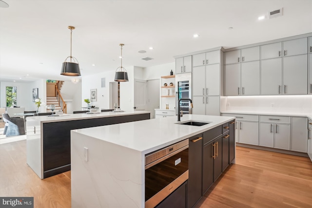 kitchen with a kitchen island with sink, sink, hanging light fixtures, and light wood-type flooring