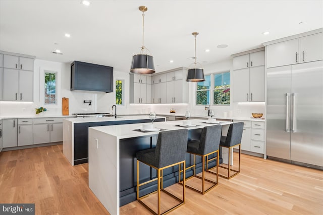 kitchen with stainless steel built in refrigerator, pendant lighting, light hardwood / wood-style floors, a kitchen bar, and a kitchen island with sink