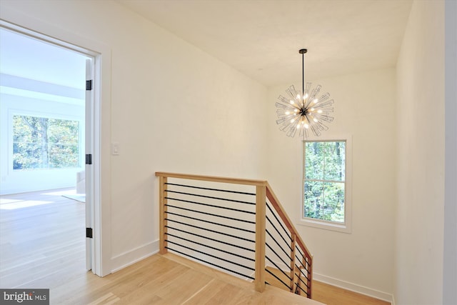 stairs featuring plenty of natural light, wood-type flooring, and an inviting chandelier